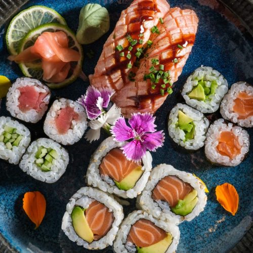 Top view of delicious assorted sushi rolls with raw salmon on plate with ginger wasabi and slices of lime on wooden table