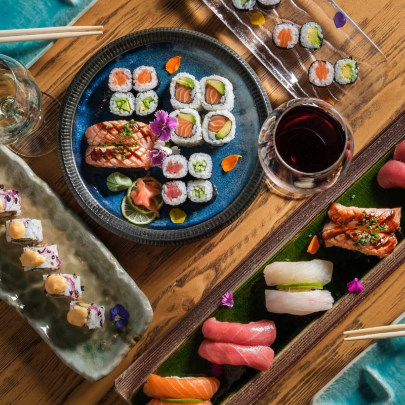 Top view of delicious various sushi and rolls with fish served on wooden table with chopsticks and wineglasses with alcohol drinks