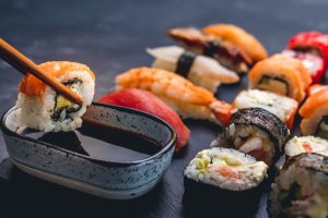 Person hold sushi maki roll with chopstick and put it to soy sauce. Oriental japanese healthy cuisine with rice and raw fish